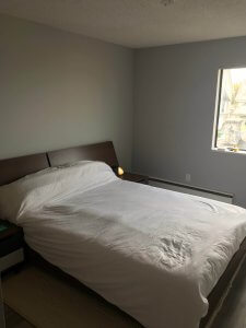 Photo of finished bedroom with a queen sized double bed with dark brown headboard and white sheets. The walls are light grey.