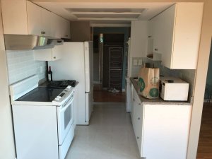 A photo looking through my galley kitchen. White appliances with white, large square tiling.