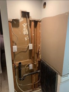 Photo of laundry area with no dry wall, bare electrics, not code-compliant plumbing, holes in walls and just generally a headache